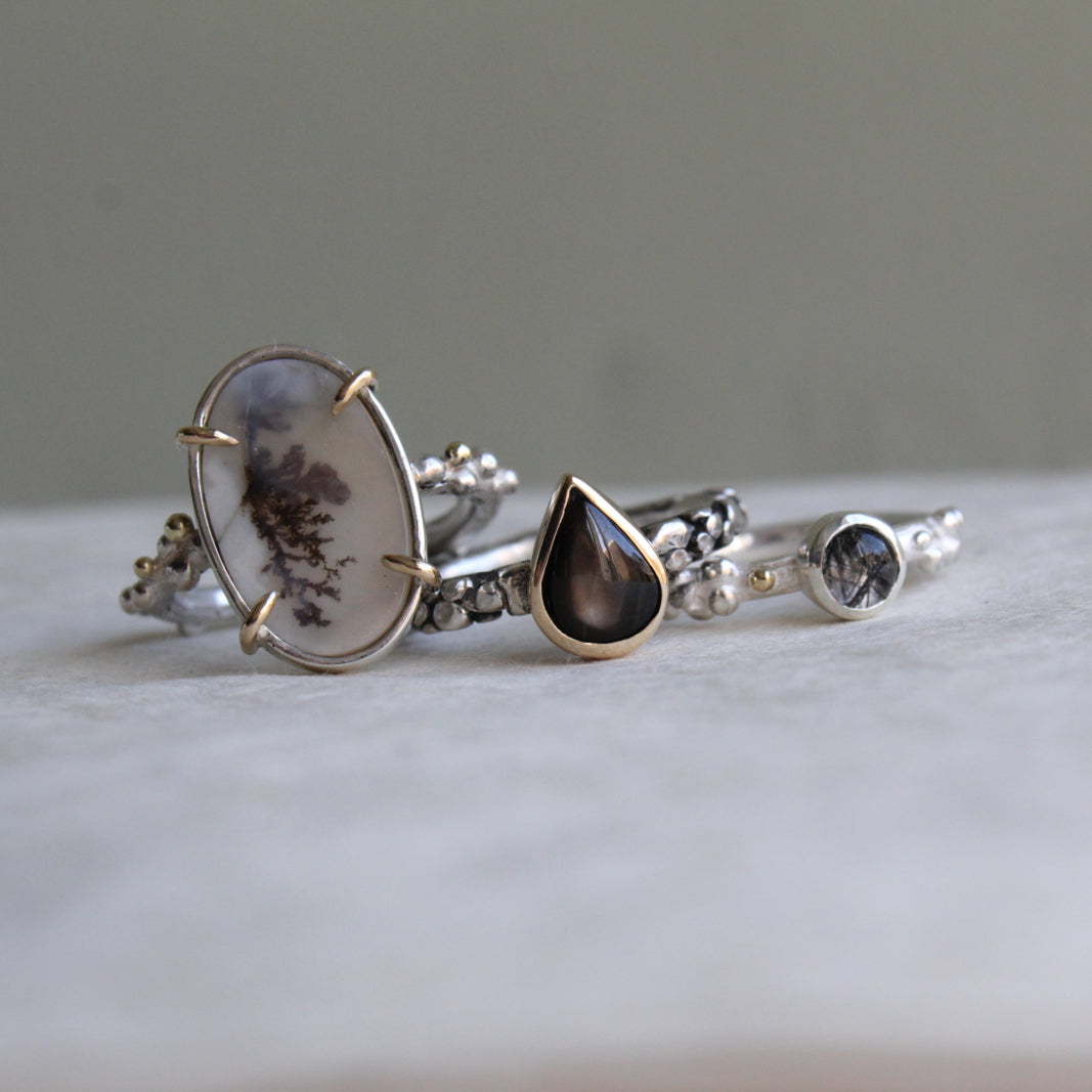verschillende ringen met neutrale edelstenen in beige en zwart.
